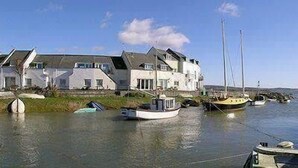 A coastal house with a large balcony overlooking the water, several boats docked nearby, and a clear sky. - Herdwicks (Millom)