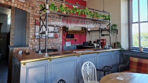 A bar area with a brick wall, hanging plants, and a bar counter with stools. - Herdwicks (Millom)