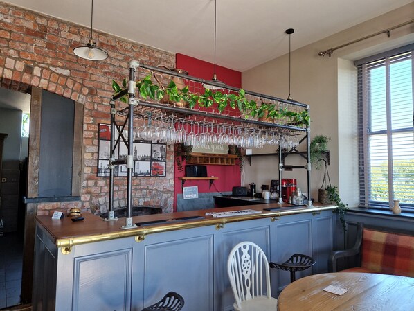 A bar area with a brick wall, hanging plants, and a bar counter with stools. - Herdwicks (Millom)