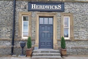 A stone building with a sign reading "Herdwicks" above a dark blue door labeled "HODDBARROW". - Herdwicks (Millom)