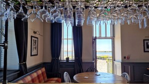 A restaurant interior with a wooden table, a sofa, and hanging wine glasses. - Herdwicks (Millom)