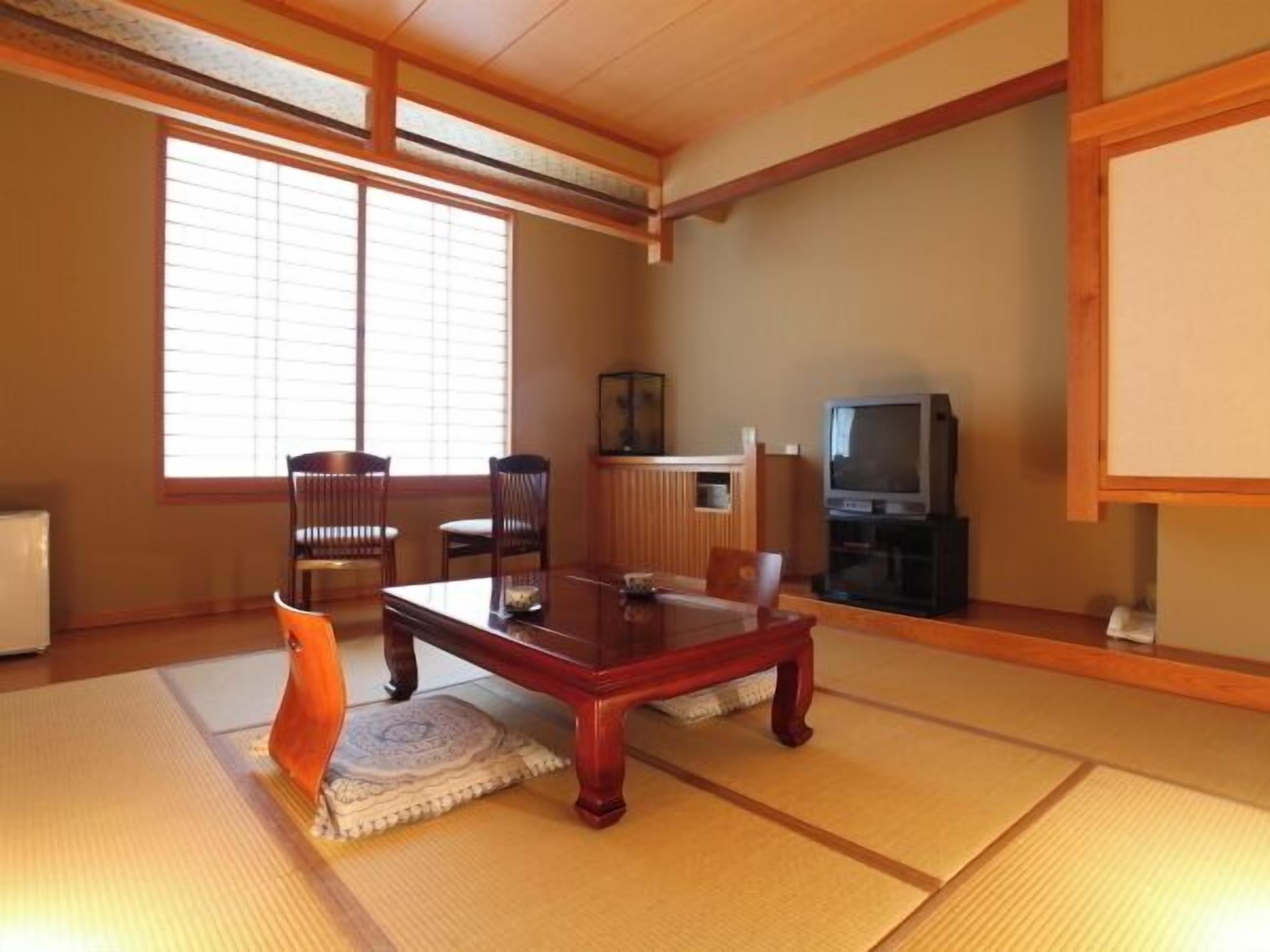 Une pièce de style japonais traditionnel, avec un sol recouvert de tatamis, une petite table en bois et un téléviseur.