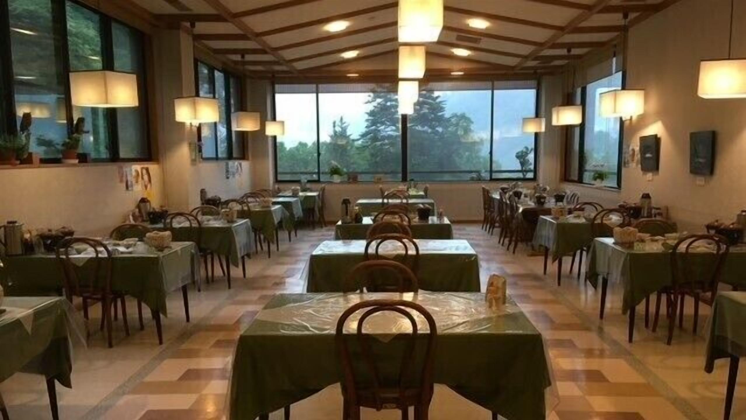 A dining area with tables and chairs, large windows, and hanging lamps.