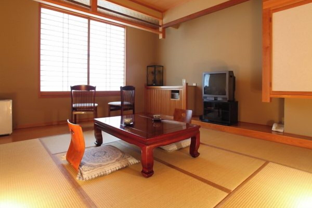Una habitación japonesa tradicional con suelo de tatami, una mesa de madera baja y un televisor.
