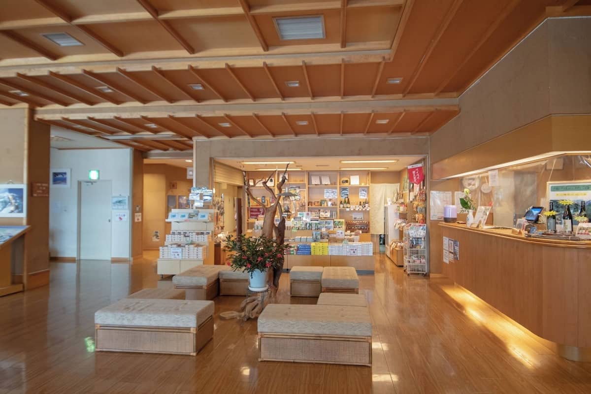 Un hall d’entrée spacieux doté d’un plancher en bois, d’un comptoir de réception, d’un espace salon et d’une vitrine où sont exposés divers objets.