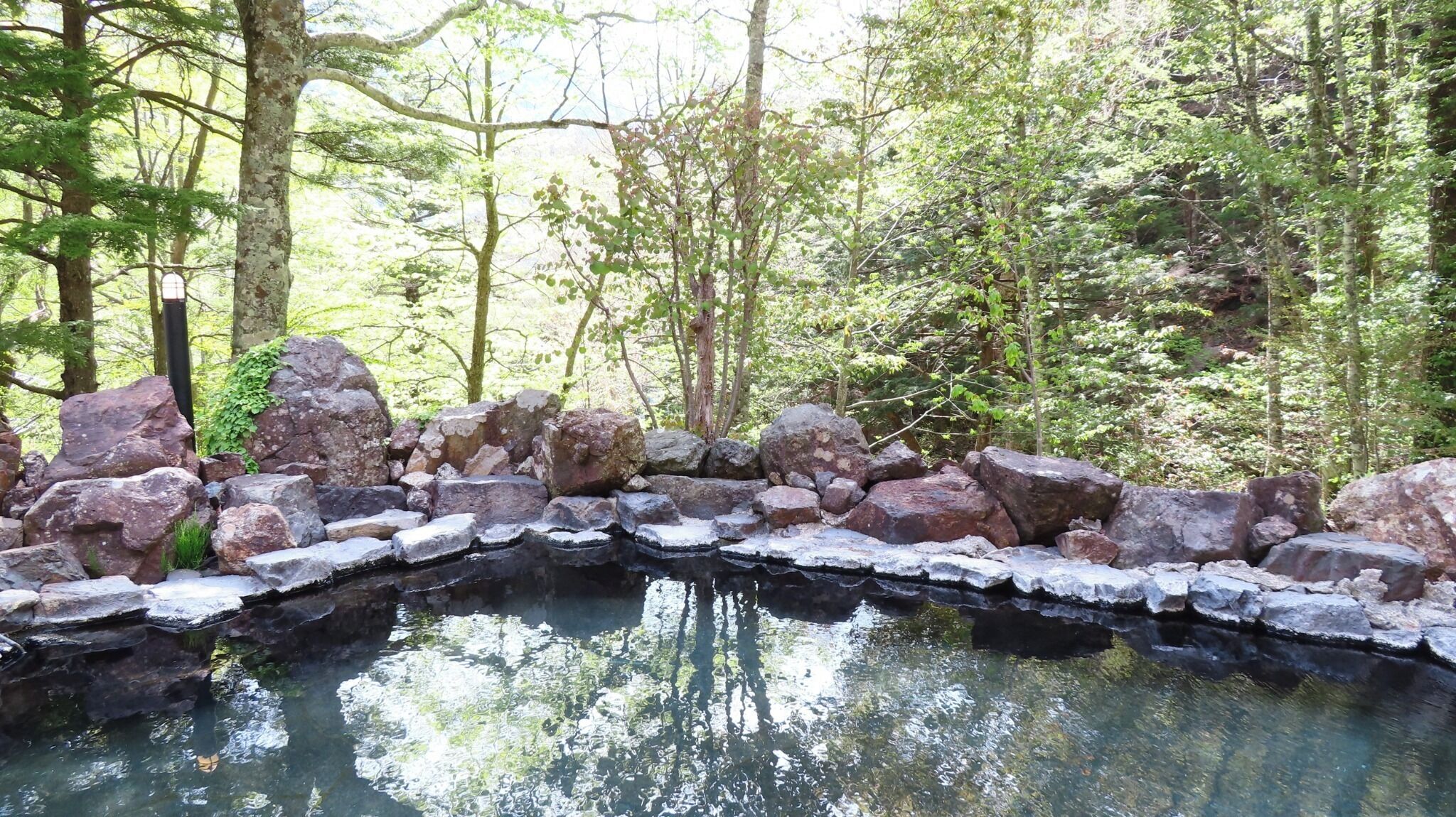 Un bassin en pierre naturelle, entouré de rochers et d’arbres.