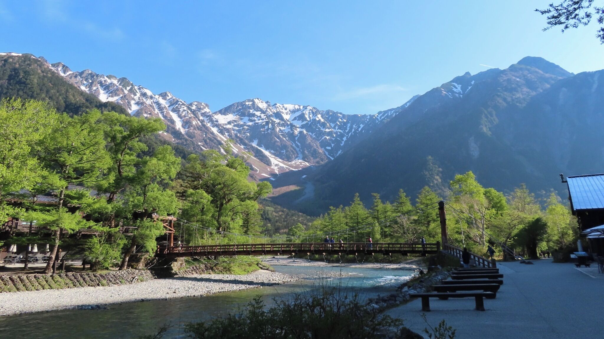 Une rivière traversée par un pont en bois, entourée d’arbres et de montagnes.