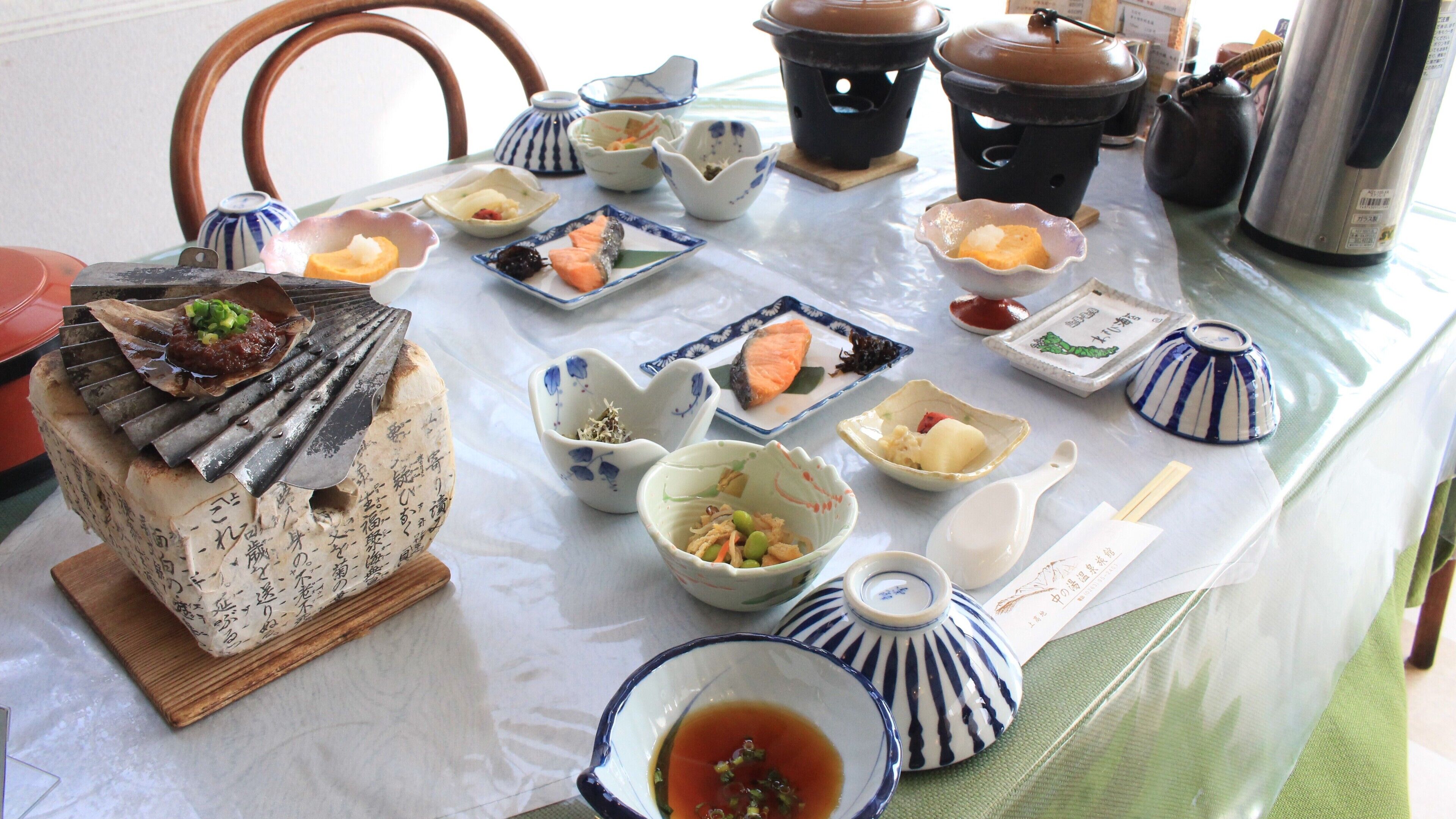A table with various dishes, including a grilled fish, bowls of soup, and a teapot.