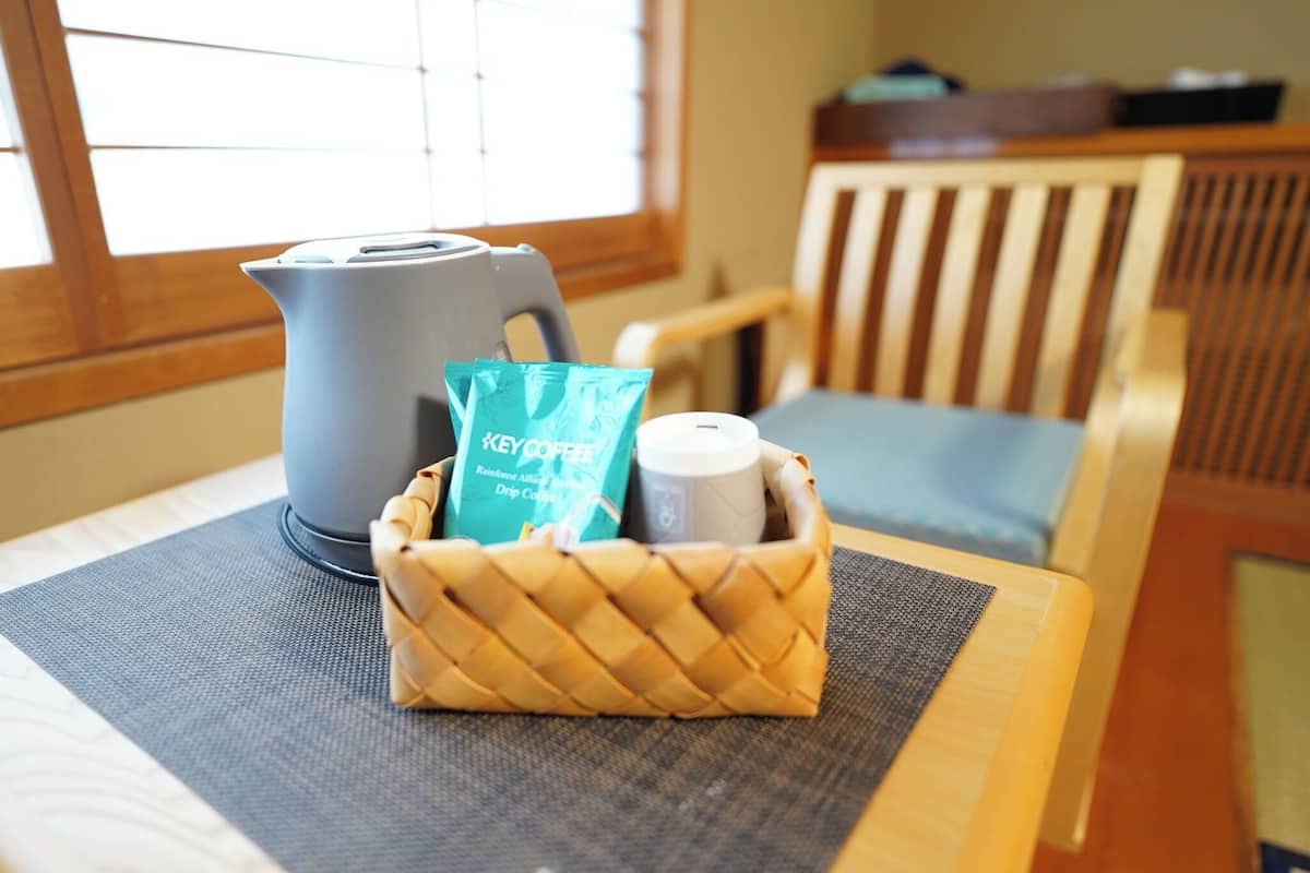 Une machine à café, un paquet de café et une bouteille sont posés sur une table, à côté d’un panier en osier.