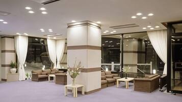 A hotel lobby with a seating area, a reception desk, and a large window.
