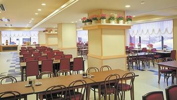 A hotel dining area with multiple tables and chairs, a checkered floor pattern, and flower arrangements on a central column.