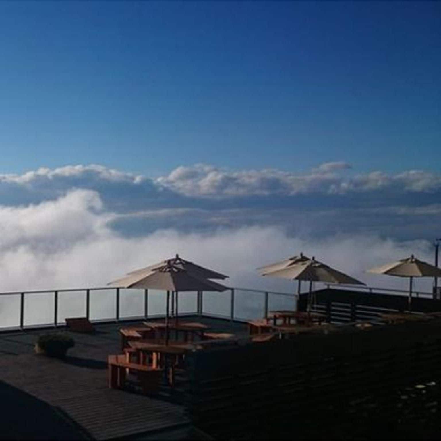 A terrace with outdoor seating and umbrellas, overlooking a cloud-covered landscape.