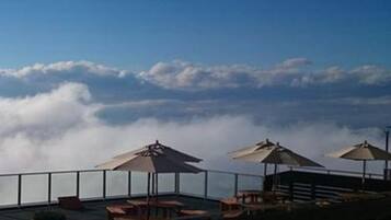 A terrace with outdoor seating and umbrellas, overlooking a cloud-covered landscape.