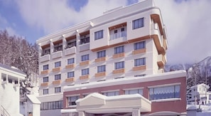 Un immeuble à plusieurs étages doté de balcons, d’un toit plat et surplombant un paysage enneigé.