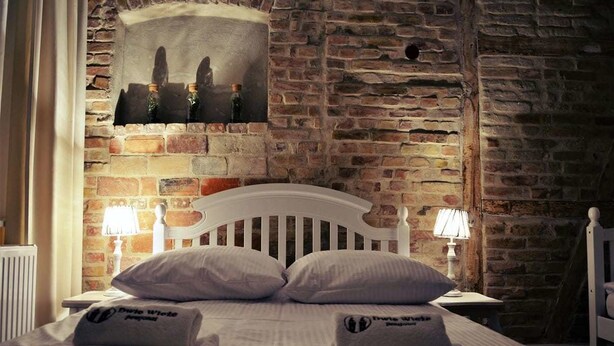 Llits amb matalasser i almoines blanques, dues làmpades de nit, una paret de maó i un quadre penjat sobre el llit.