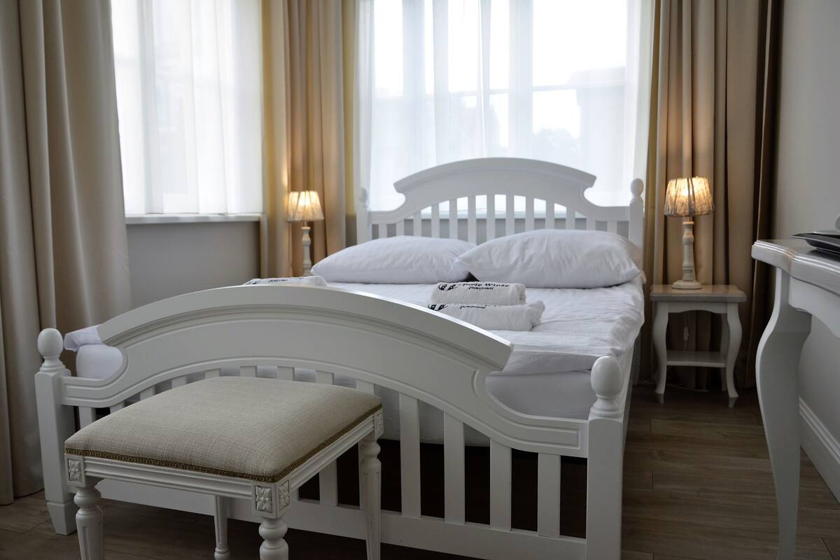 Een netjes ingerichte slaapkamer met een wit bed, een nachtkastje met een lamp en een stoel.