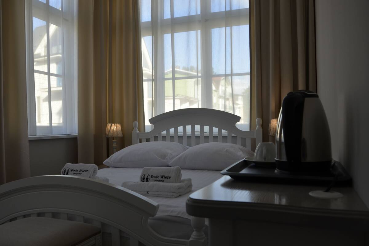 Een hotelkamer met een bed, een nachtkastje met een waterkoker en een raam met gordijnen.