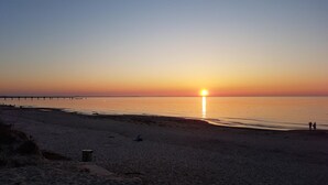 Una platja amb un moll que s'endinsa en aigües tranquil·les durant el capvespre.