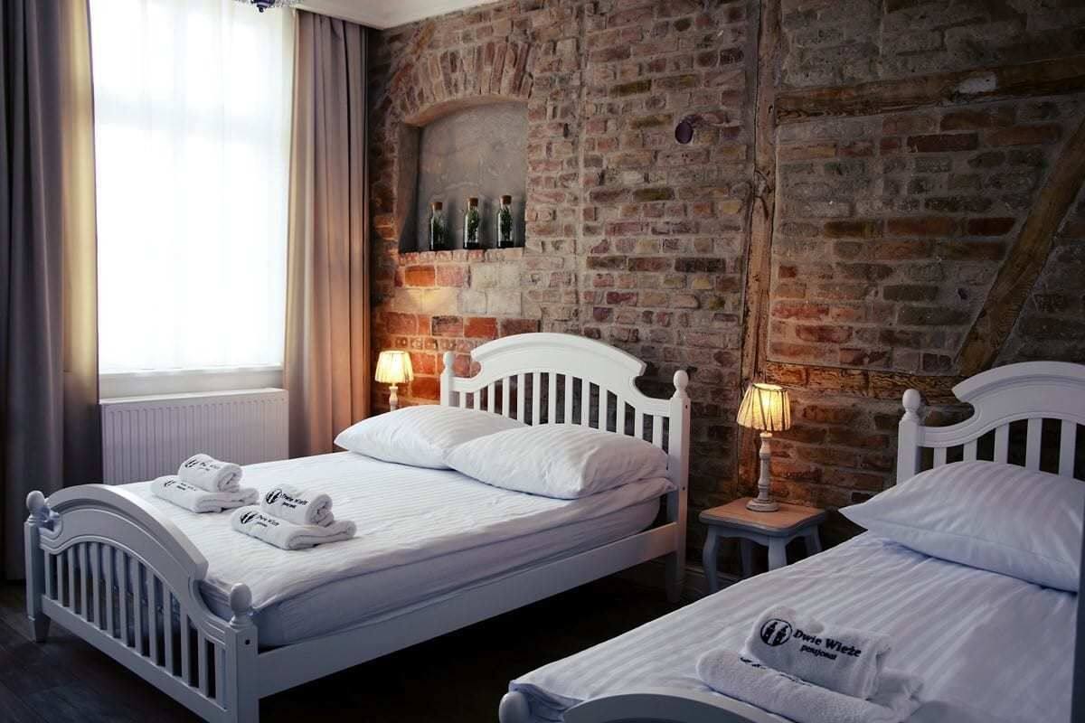 Een hotelkamer met twee bedden, een bakstenen muur en een raam met gordijnen.