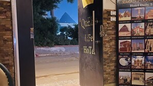 A hotel entrance with a door labeled 'Queen Life Hotel' and a poster of the Pyramids of Giza. - Makadi Pyramids View (Giza)