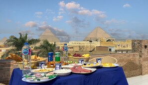 A table set with various food items and drinks, with the pyramids in the background. - Makadi Pyramids View (Giza)