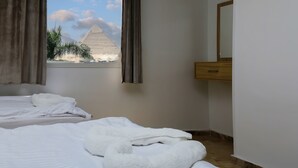 A hotel room with two beds, a window with a view of the pyramid, and a wooden nightstand. - Makadi Pyramids View (Giza)