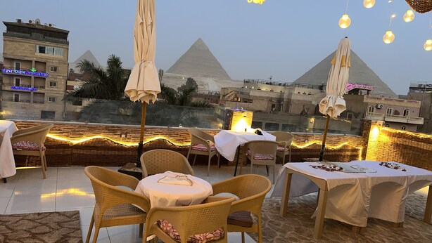An outdoor dining area with wicker chairs and tables, overlooking the pyramids. - Makadi Pyramids View (Giza)