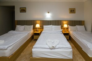 A hotel room with three single beds, each with a wooden headboard and a nightstand with a lamp. The room has a neutral color scheme and a simple, clean design. - Makadi Pyramids View (Giza)
