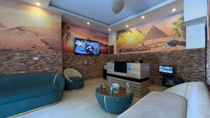 A living room with a stone wall, a flat-screen TV, a sofa, a chair, and a coffee table. - Makadi Pyramids View (Giza)