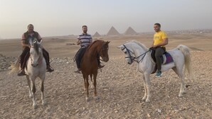 Three people riding horses in a desert landscape with pyramids in the background. - Makadi Pyramids View (Giza)