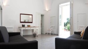 Ein geräumiges Wohnzimmer mit zwei schwarzen Sofas, einem weißen Konsolentisch und einem großen Spiegel.