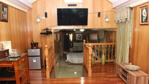 A wooden interior with a TV mounted on the wall, a wooden staircase, and a bed in the background.