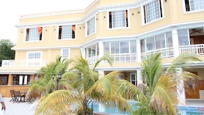 A multi-story hotel with a pool area, palm trees, and a balcony with a railing.