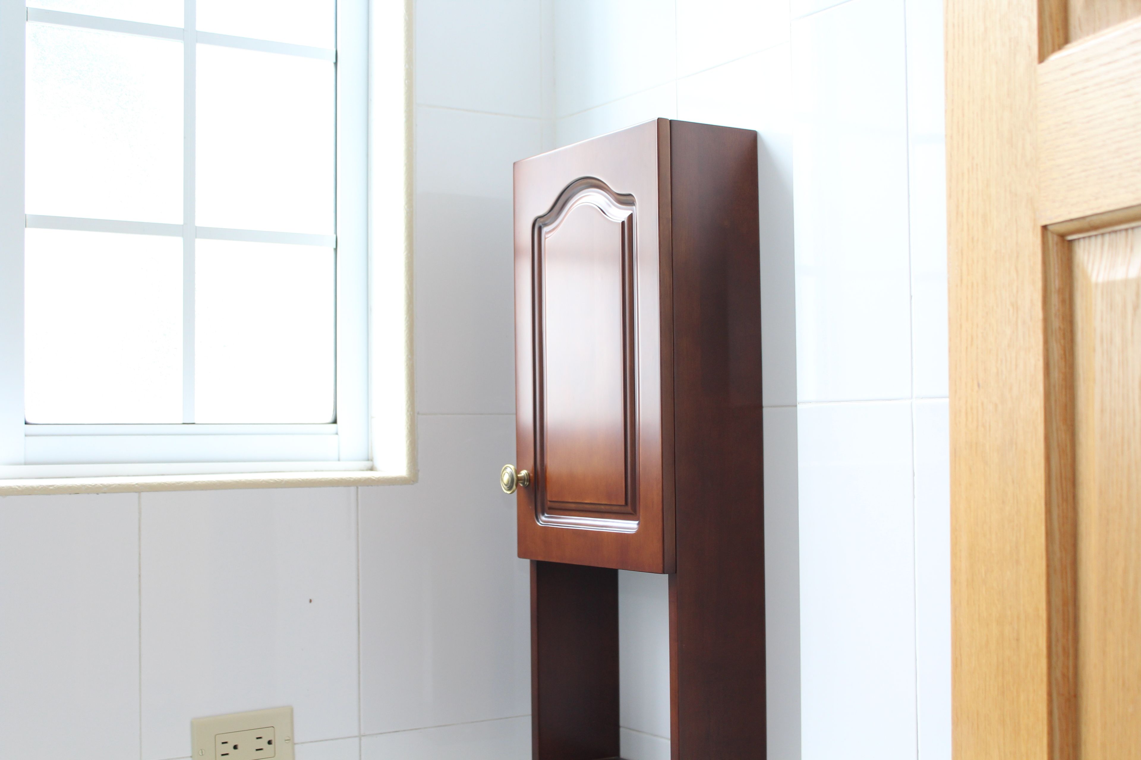 A wooden cabinet with a door in a room with white walls and a window.