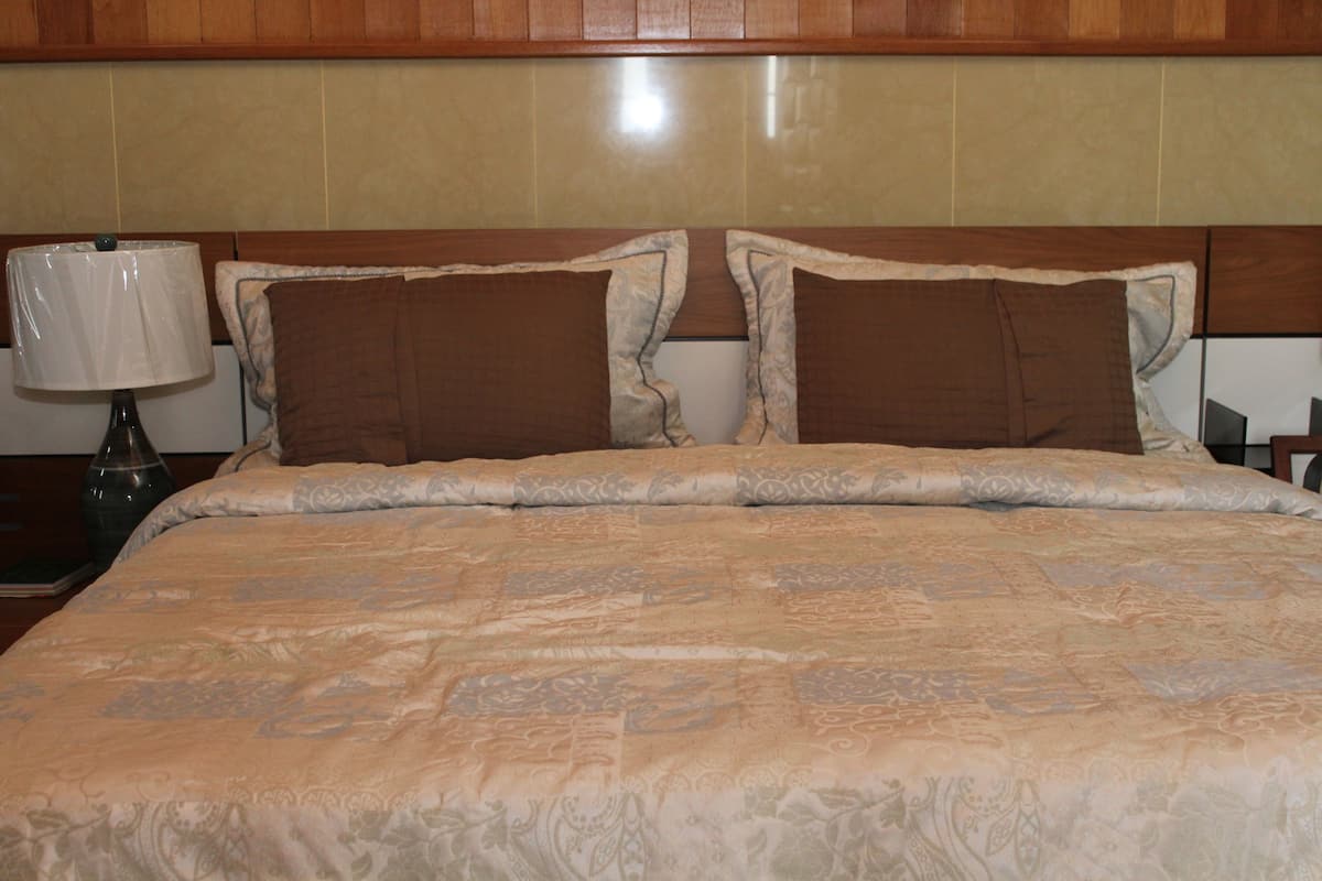 A neatly made bed with a patterned bedspread and two pillows, a bedside lamp, and a wooden headboard.