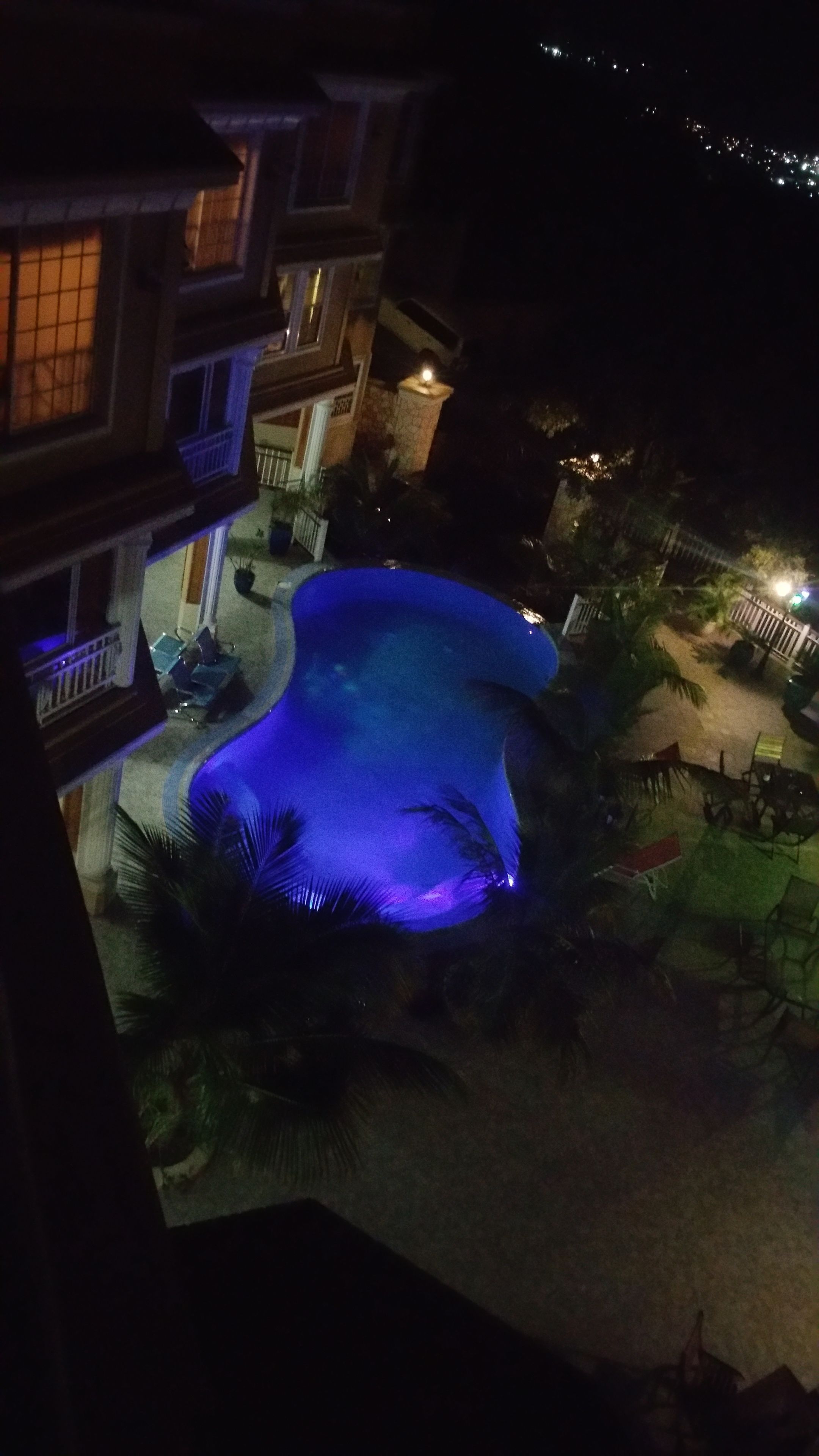 Een nachtzicht van een hotel binnenplaats met een zwembad, palmbomen en terrasmeubilair.