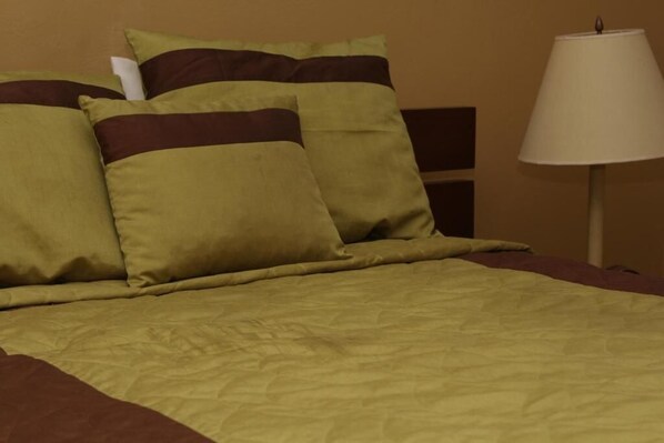 Una cama con un edredón verde y marrón, dos almohadas y una lámpara de noche.