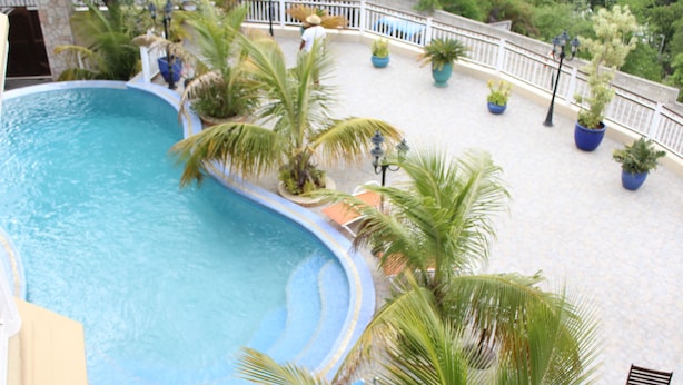 A pool area with a curved edge, surrounded by potted plants and a white railing.
