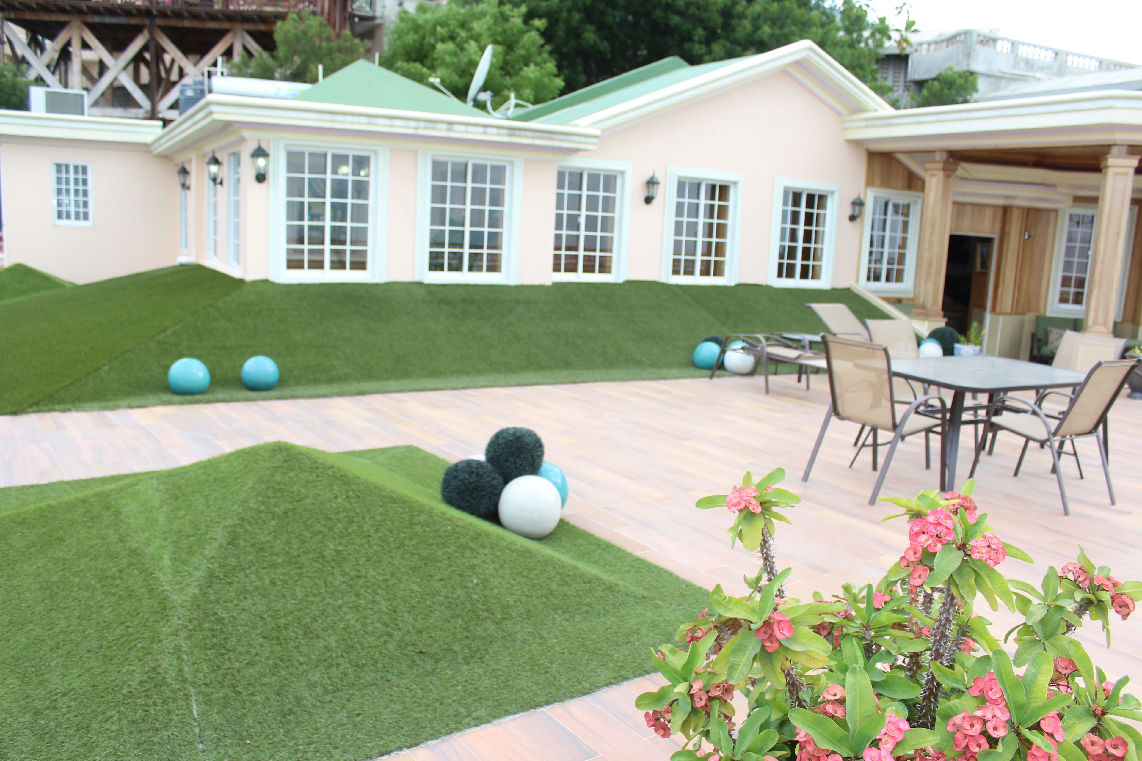 A patio area with artificial grass, a table with chairs, and a building with multiple windows and doors.