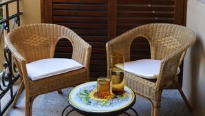 Two wicker chairs with white cushions, a small round table with a floral tablecloth, and a glass of amber liquid. - Re Ruggero Rooms (Reggio Calabria)