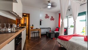 Een compacte hotelkamer met kitchenette, een bed met baldakijn, een eethoek en een kleine televisie.