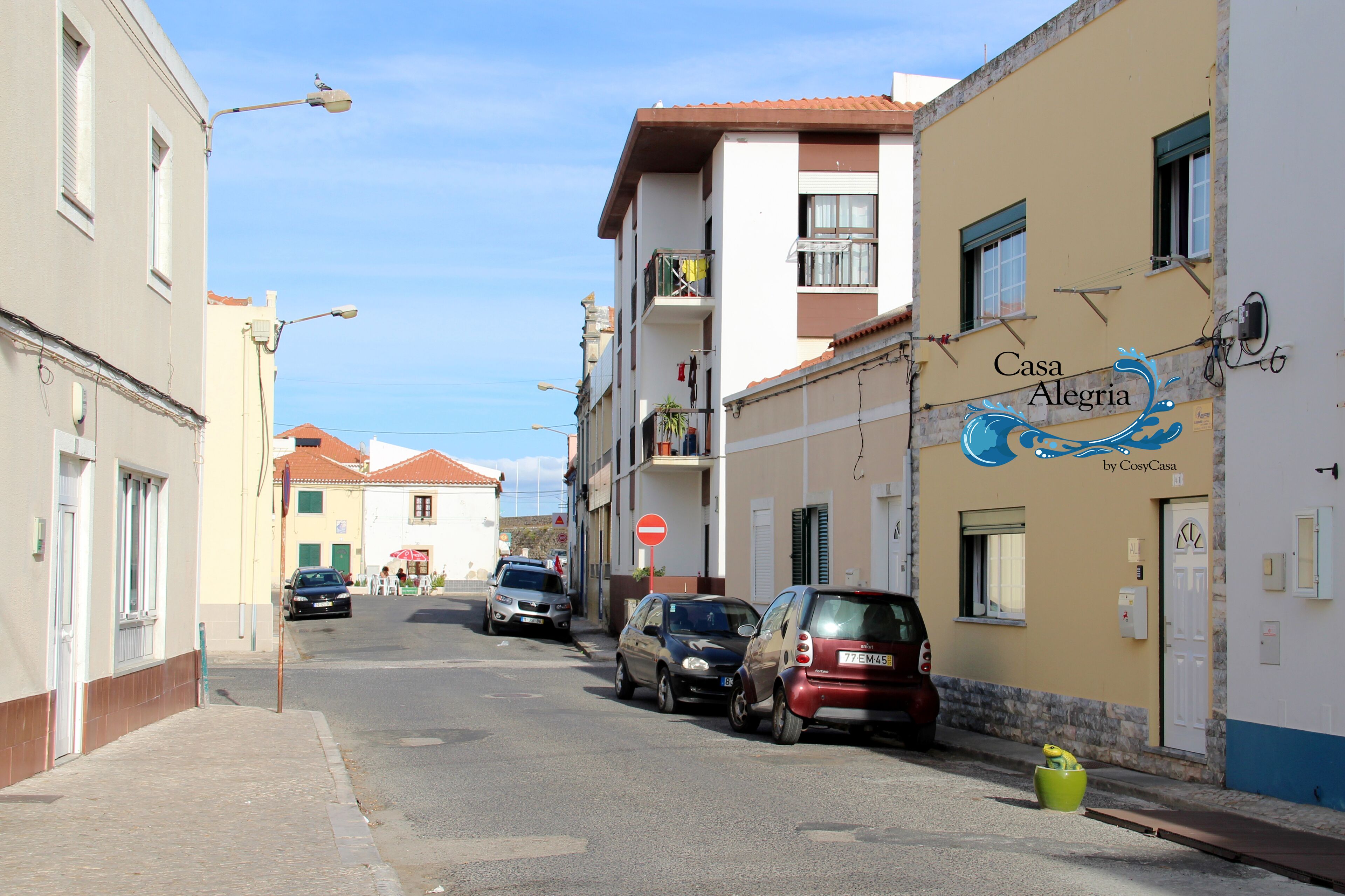 A street with parked cars and buildings, including a property named 'Casa Alegre' with a sign indicating it's by CosyCasa.