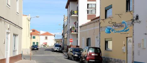 A street with parked cars and buildings, including a property named 'Casa Alegre' with a sign indicating it's by CosyCasa.