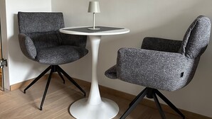 A modern room with a round white table, two grey upholstered chairs, and a painting of a landscape on the wall.