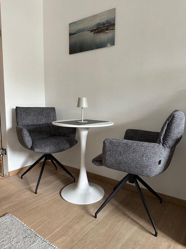 A modern room with a round white table, two grey upholstered chairs, and a painting of a landscape on the wall. - Luxury holiday apartment Tegernsee - Design Ferienappartement Tegernsee (Tegernsee)