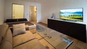 A modern living room with a sofa, a glass coffee table, and a television displaying a scenic landscape.