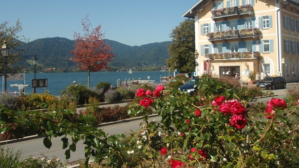 A hotel with a balcony overlooking a lake, surrounded by lush gardens and a clear sky.