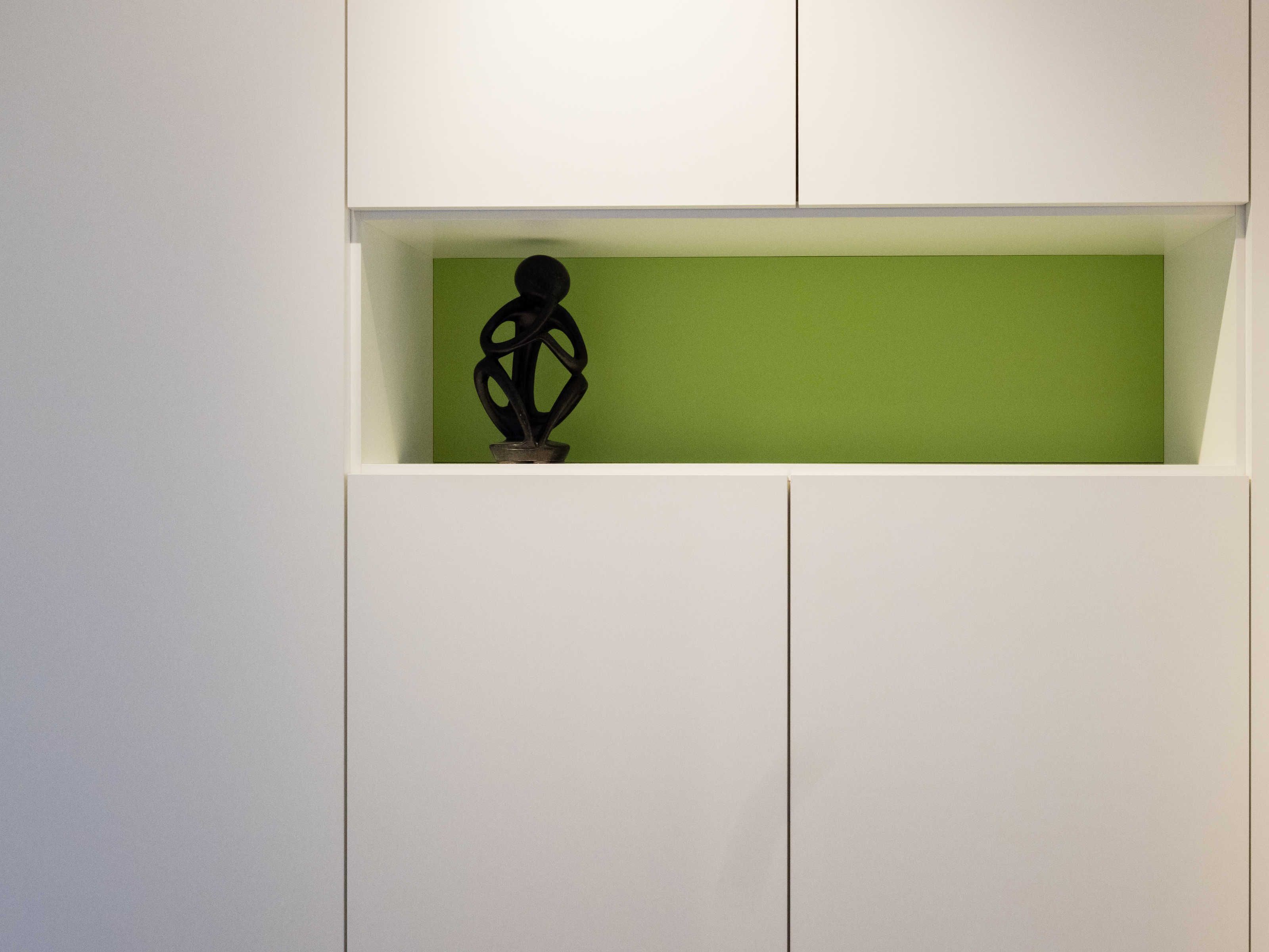 Ein weißes Schranksystem mit einem grünen Regal, das eine schwarze, abstrakte Skulptur beherbergt.