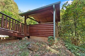 A wooden cabin with a covered porch, surrounded by a forested area.