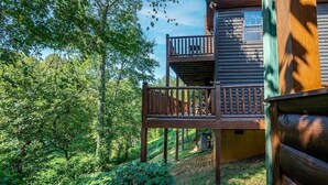 A wooden cabin with a balcony, surrounded by dense forest. - Paw Prints (Sevierville)